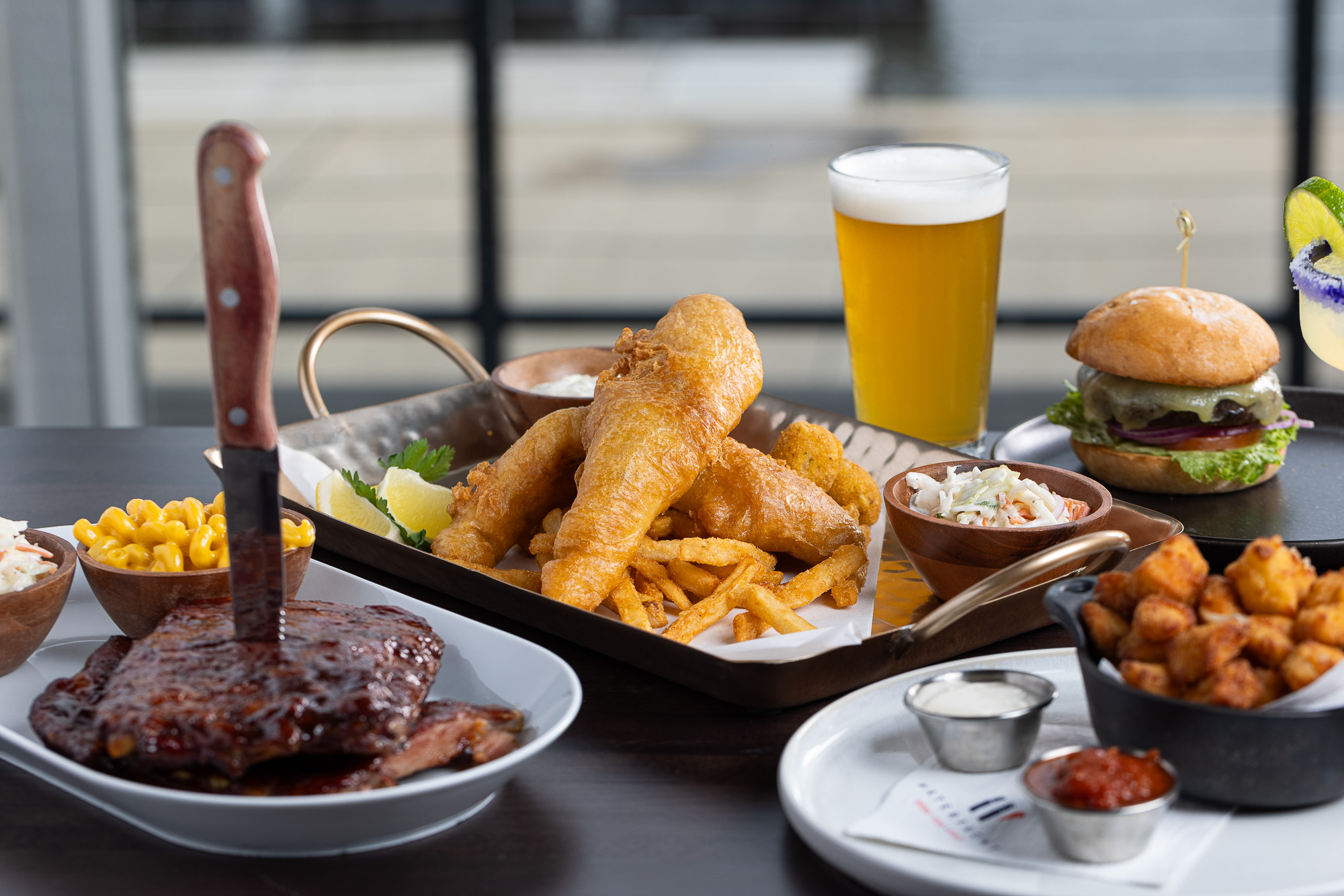 Spread of fish fry, ribs, burger and beer on the deck